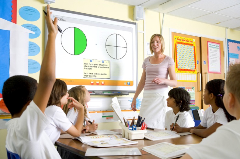 An elementary teacher discusses fractions with students seated at classroom tables.